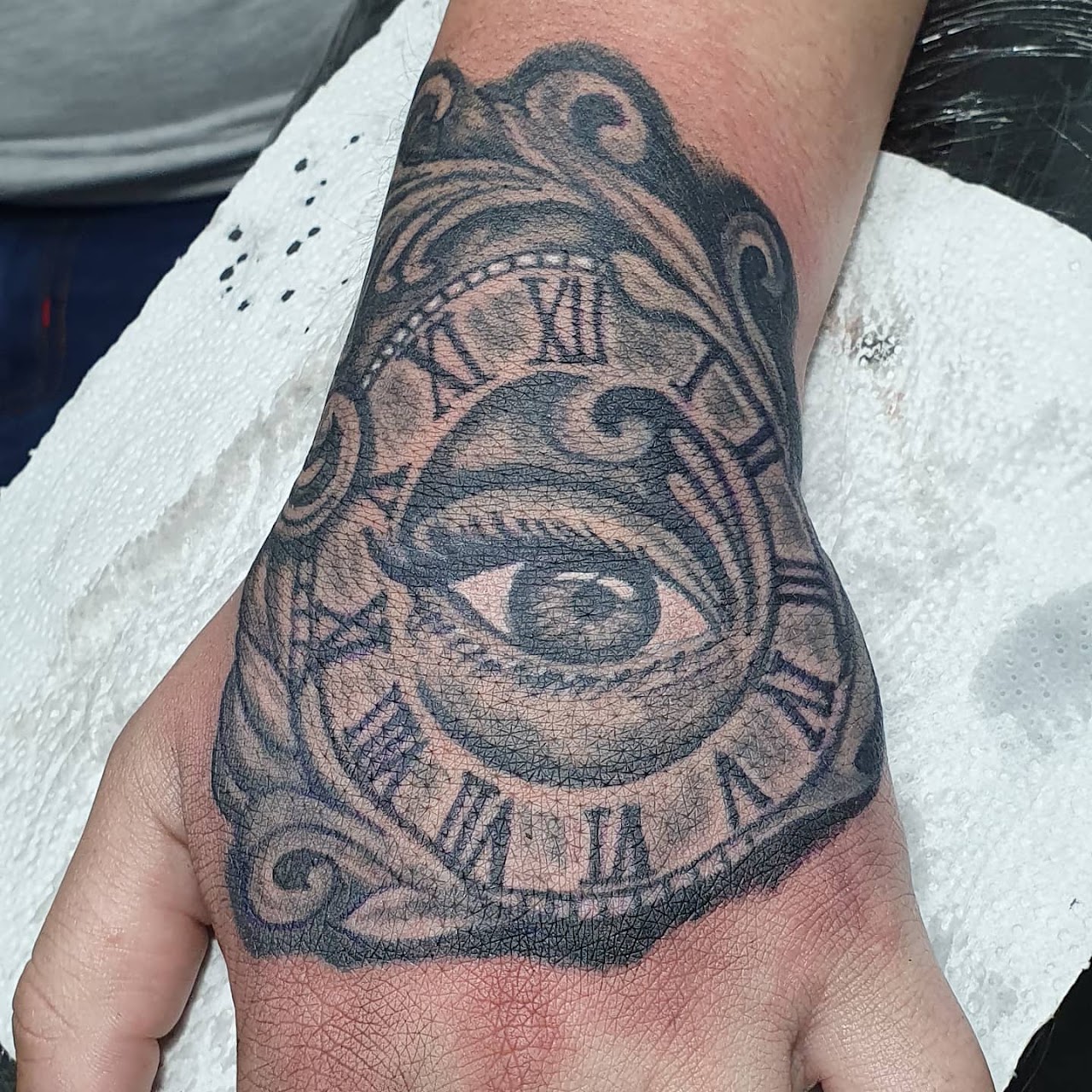 Tatuaje blackwork de ojo y reloj en la mano, realizado en Tattoo Pappa